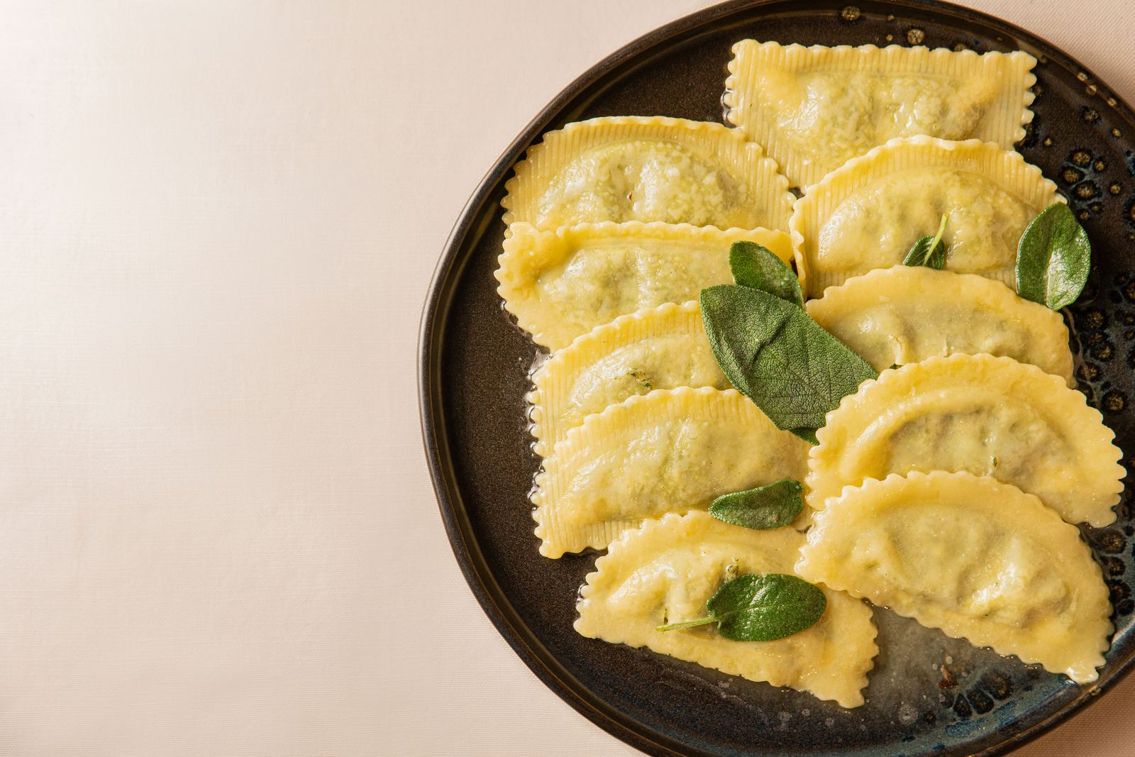 Ravioli fatti in casa con foglie di salvia su piatto scuro